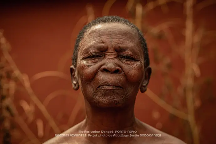 Âgé plus de soixantaine, IYA fait partie des femmes du couvent. Porto-novo, Bénin. 2024.  Dans le culte vodoun, les femmes possèdent dans l'ombre le secret de plusieurs rituels. Même si l'homme semble prendre les devants dans le monde vodoun, la femme incarne la force spirituelle de tout ce qui se fait.